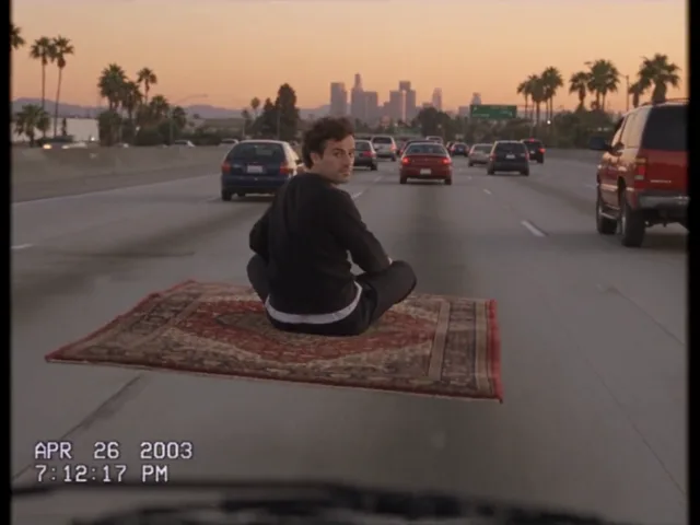 Ein Mann sitzt im Schneidersitz auf einem Perserteppich, der zwischen den Fahrspuren eines Freeways schwebt, im Hintergrund die Skyline von Los Angeles