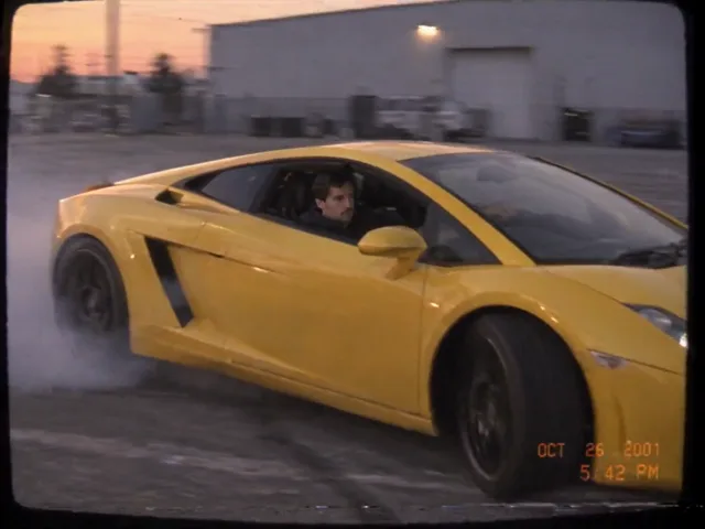 Ein gelber Lamborghini steht quer auf einem leeren Betonplatz, unter den Hinterrädern steht Reifenrauch, dahinter der Sonnenuntergang