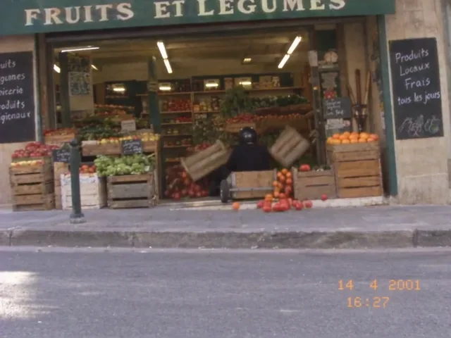 Eine Holz-Seifenkiste ist in die Obstkisten vor einem französischen Gemüseladen gefahren, Tomaten rollen über den Gehweg auf die Straße