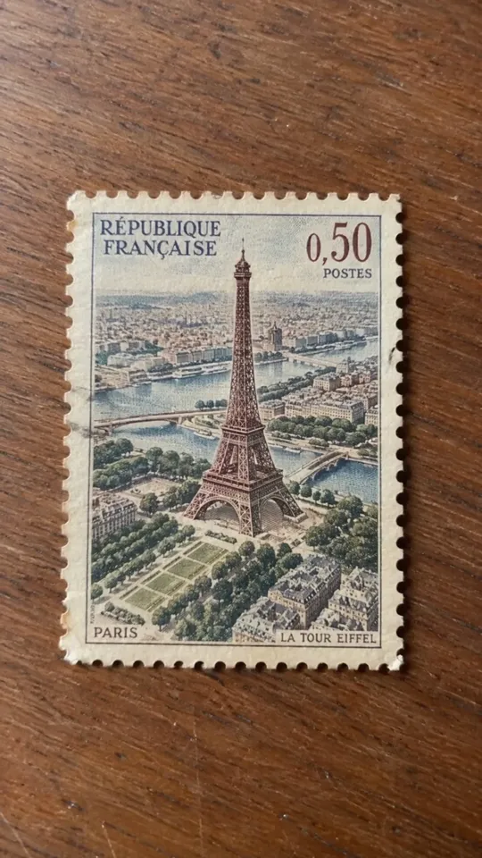 Die gestochene Eiffelturm-Briefmarke liegt flach auf dem Holztisch, Perforation und Papierfasern sichtbar