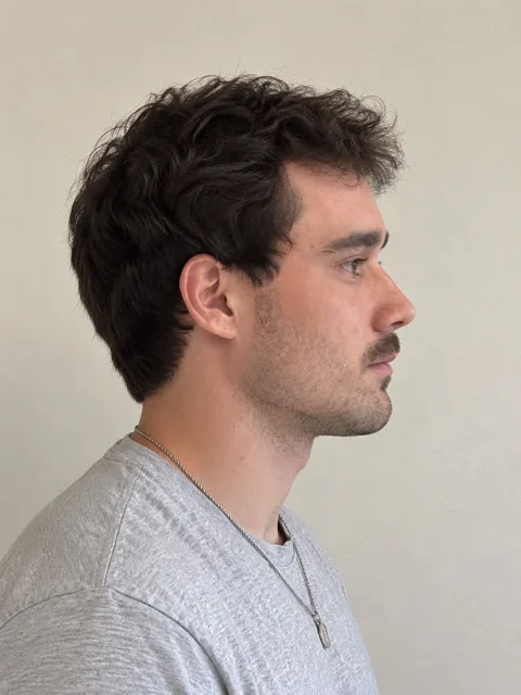 Dieselbe Person im reinen Profil vor neutralem Hintergrund, gleiches graues T-Shirt und gleiche Kette