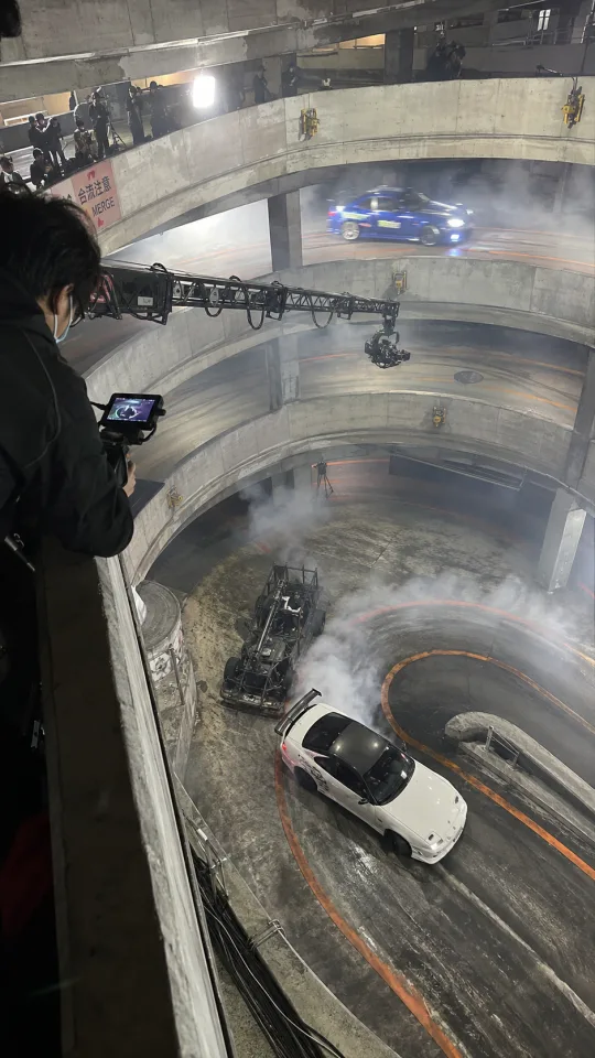 Keyframe 1: Blick von oben über das Geländer ins Parkhaus, Kamerakran und Crew im Bild