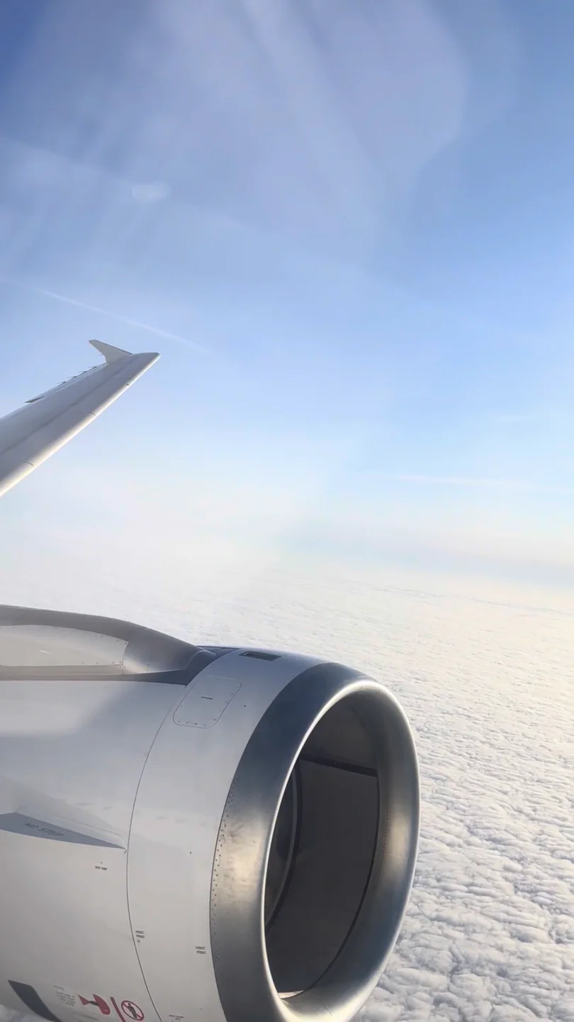 Handyfoto aus einem Flugzeugfenster: Tragflächenspitze links oben, Triebwerk links unten, darunter eine geschlossene Wolkendecke bis zum Horizont