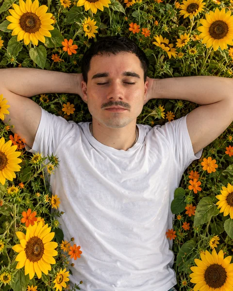 Das erzeugte Bild aus der Vogelperspektive: derselbe Mann liegt mit den Händen hinter dem Kopf in einem dichten Feld aus Sonnenblumen und orangen Wildblumen
