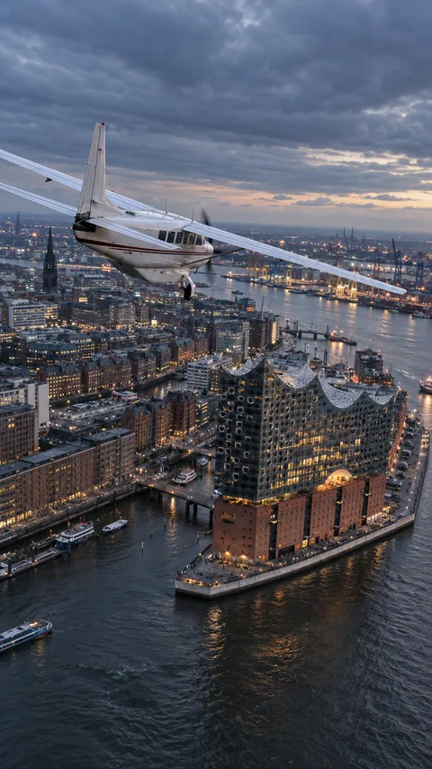 Die Maschine zieht über die beleuchtete Elbphilharmonie und die Speicherstadt, die Elbe und der Hafen liegen im letzten Tageslicht