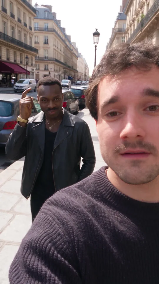 Selfie-Ansicht: hinter dem Vlogger tippt sich ein Mann in schwarzer Lederjacke im Vorbeigehen an die Schläfe